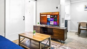 Una sala de estar moderna con un televisor de pantalla plana mostrando servicios de transmisión, una mesa de centro de madera y un sofá.