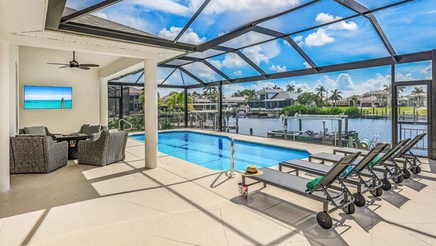 A covered outdoor swimming pool area with lounge chairs and a ceiling fan. - Luxe Home, Pool, Boat Rental, Hot tub, & Fire pit (Cape Coral)