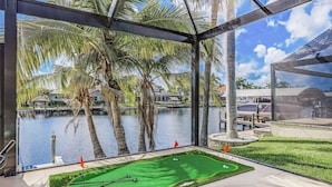 A golf putting green with a view of a lake and palm trees. - Luxe Home, Pool, Boat Rental, Hot tub, & Fire pit (Cape Coral)