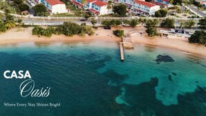 Vista aérea de uma área costeira com um hotel, vários edifícios, uma praia e um cais.