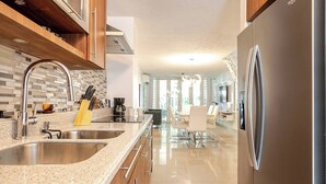 Uma cozinha moderna com bancadas de granito, eletrodomésticos de aço inoxidável e uma área de jantar com cadeiras brancas.