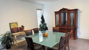 A dining room with a glass table, wooden chairs, a large wooden cabinet, a small Christmas tree, and a potted plant. - Big Beautiful house in Richmond centre (Richmond)