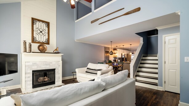 Sala de estar con chimenea, sofá y televisor. Una escalera conduce a una zona de cocina.