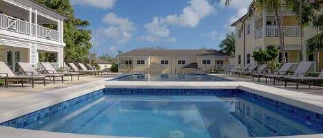 A swimming pool with lounge chairs, a building with balconies, and palm trees.