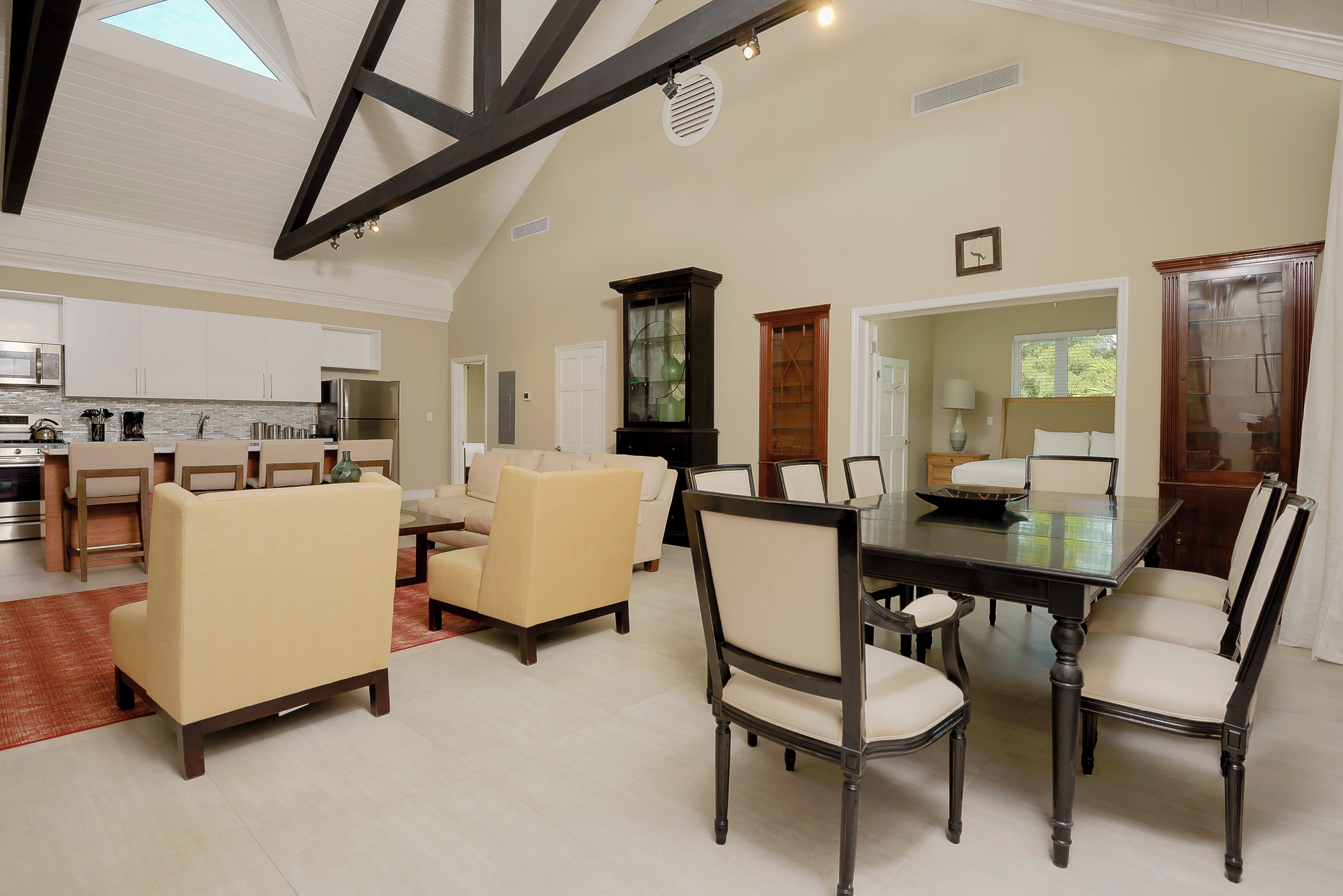 A spacious living area with a high ceiling, a dining table with chairs, a sofa, and a kitchen in the background.