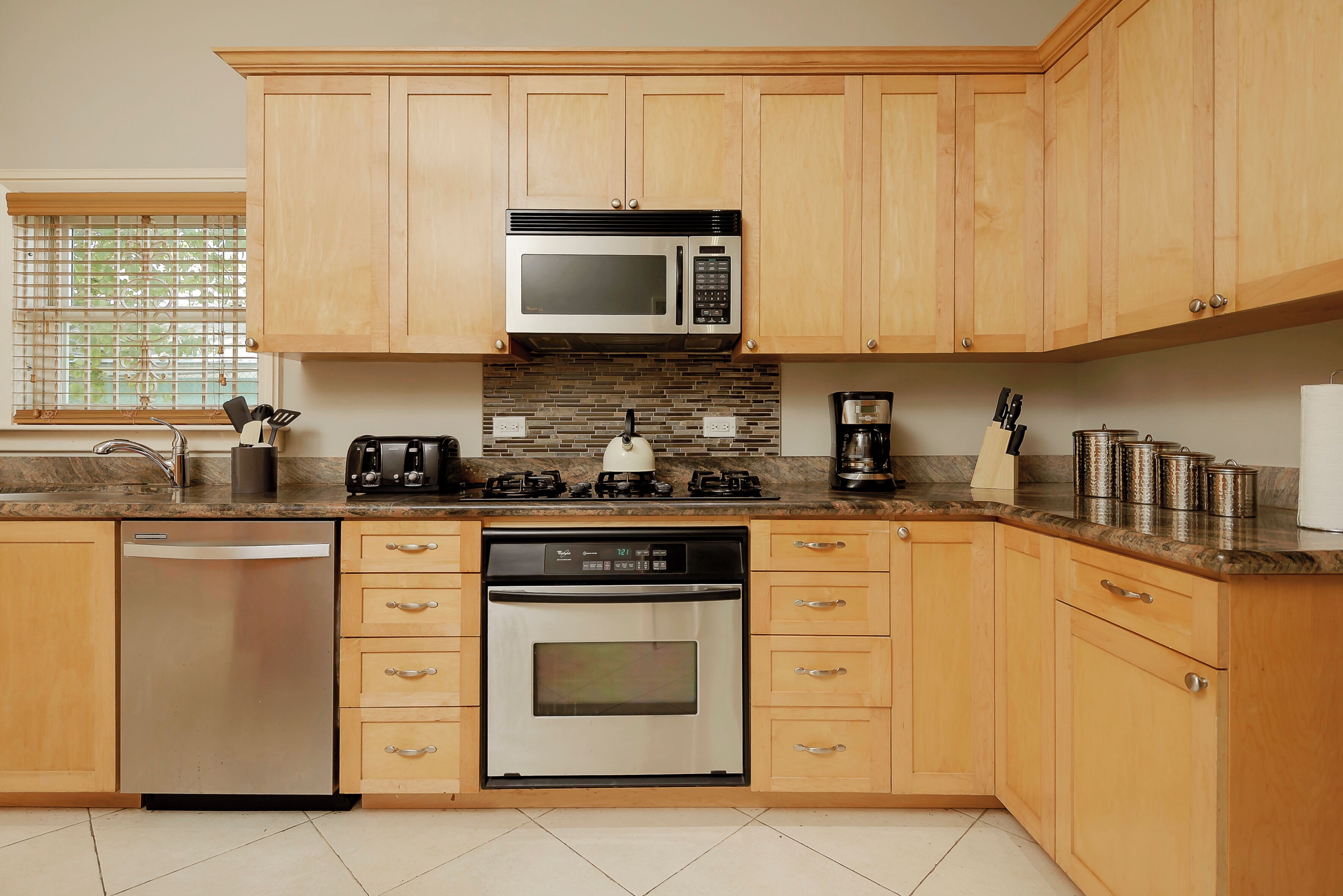 Una cocina moderna con armarios de madera, un lavavajillas de acero inoxidable, horno integrado, microondas, estufa a gas y cafetera.