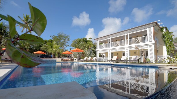 Uma área de piscina com um edifício de dois andares, cadeiras de lounge e guarda-sóis.
