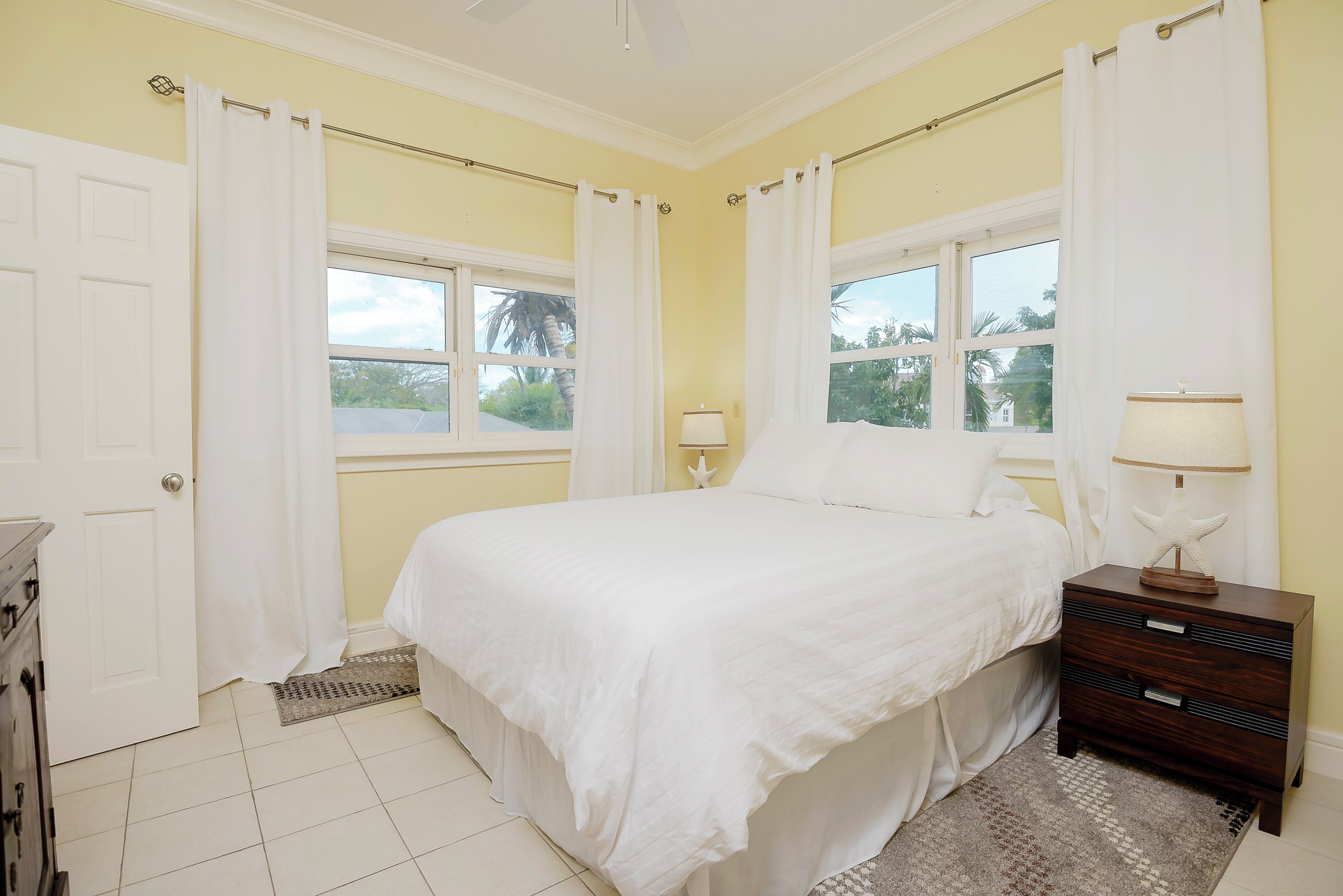 Un dormitorio con cama, mesita de noche, lámpara y ventana con cortinas.