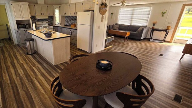 Una cocina moderna con una isla central, un comedor con una mesa redonda y una sala de estar con sofá y mesa de centro.
