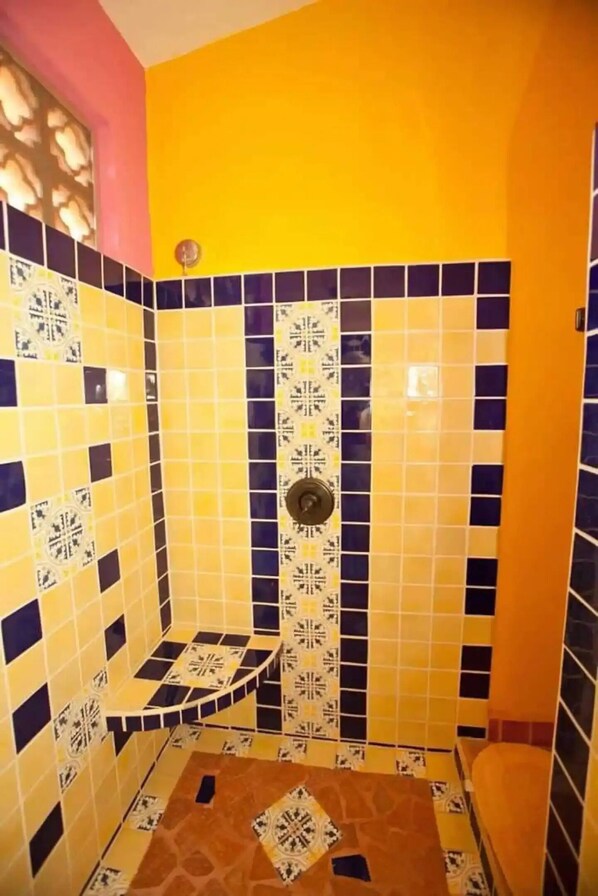 Un baño con azulejos estampados en amarillo y azul, una zona de ducha y un inodoro.