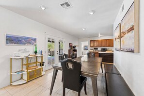 A modern kitchen with wooden cabinets, a dining area with a dark wood table and leather chairs, and a view through glass doors to an outdoor area.