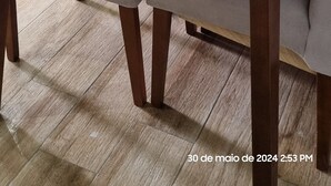 A dining area with a glass-top table and cushioned chairs, a decorative wall with floral patterns, and a kitchen in the background. - Luxuoso AP no Martim Praia Clube - Martim de Sá (Martim de Sá Caraguatatuba)