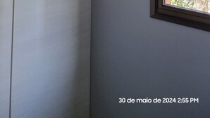 A room with a built-in air conditioning unit, a window with a view of a residential area, and a door. - Luxuoso AP no Martim Praia Clube - Martim de Sá (Martim de Sá Caraguatatuba)
