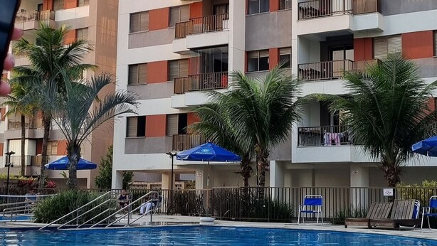 A swimming pool with lounge chairs and umbrellas, surrounded by a multi-story building with balconies. - Luxuoso AP no Martim Praia Clube - Martim de Sá (Martim de Sá Caraguatatuba)