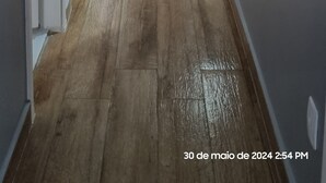 A narrow hallway with a wooden floor leading to a kitchen area. A dining table with chairs is visible on the left, and a refrigerator is in the kitchen. - Luxuoso AP no Martim Praia Clube - Martim de Sá (Martim de Sá Caraguatatuba)
