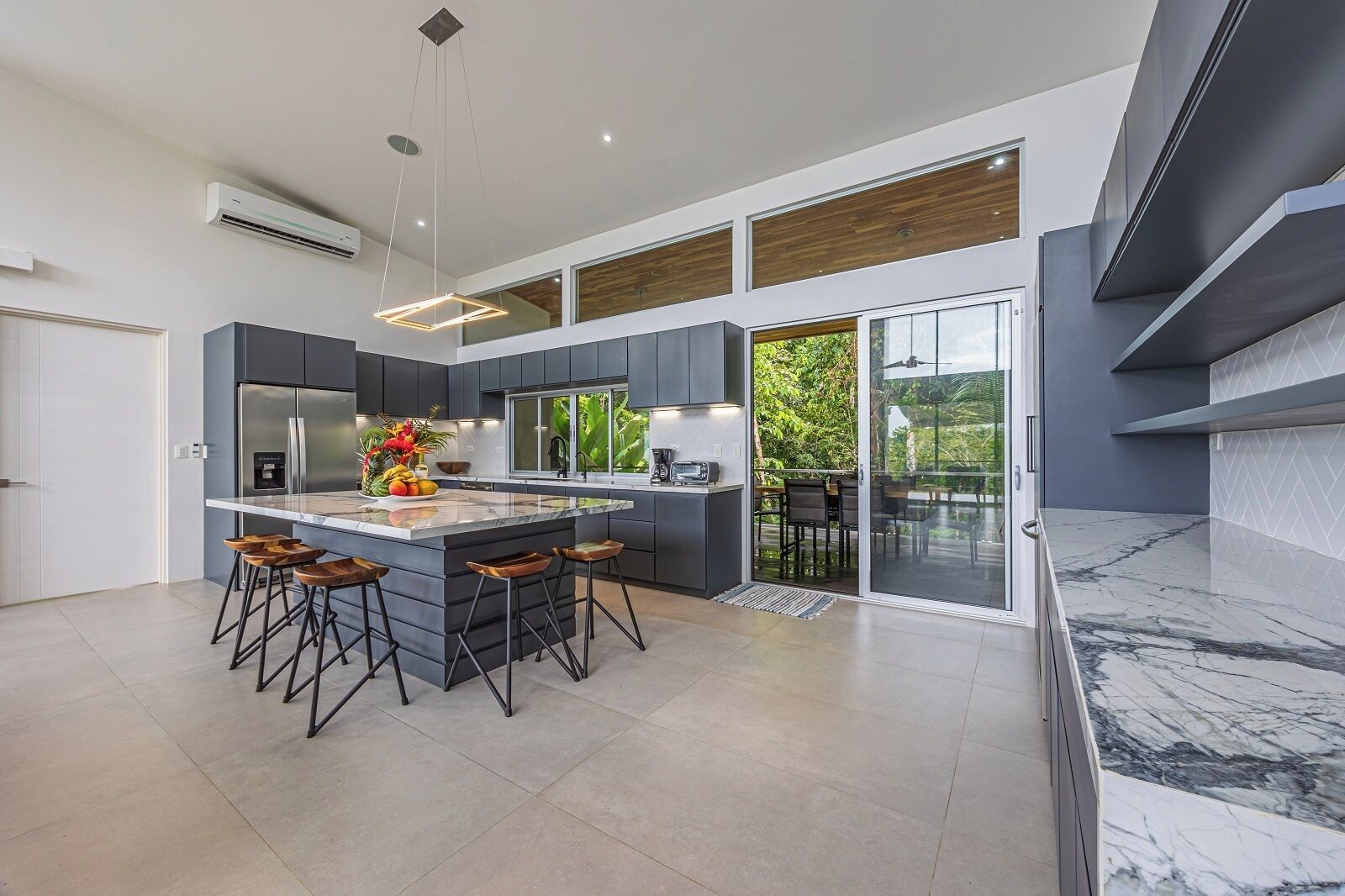 Cozinha moderna com uma ilha grande, armários escuros e vista para um deck externo.