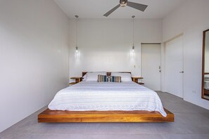 Un dormitorio moderno con una cama grande, dos lámparas colgantes, un ventilador de techo y una cama con plataforma de madera.