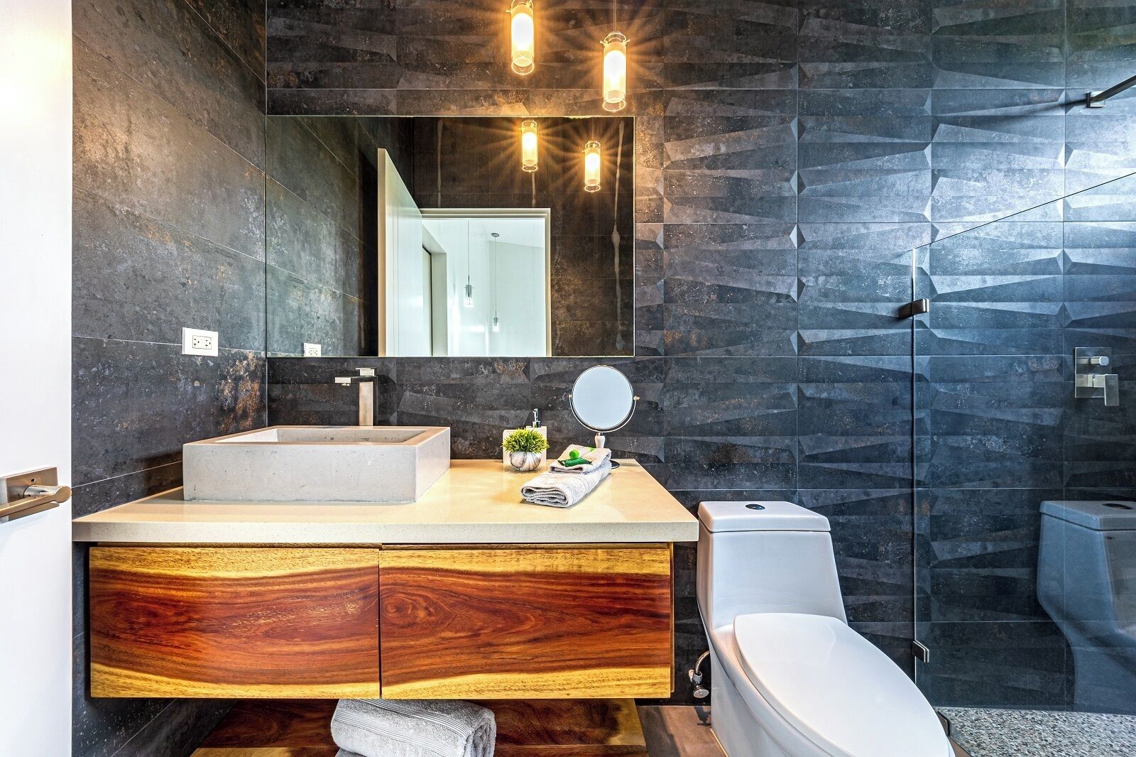 Un bany modern amb un mirall gran, un lavabo de fusta, un rentapeus blanc i un vàter.
