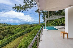 Un balcón con piscina, rodeado de exuberante vegetación y vistas al océano.
