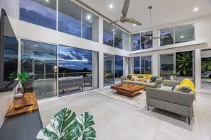 Amplia sala de estar con un ventanal que ofrece una vista panorámica, ventilador de techo y un moderno juego de sofás.