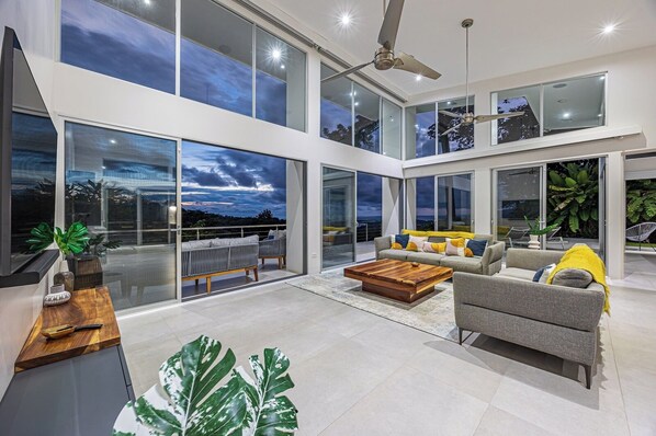 A spacious living area with a large window overlooking a scenic view, a ceiling fan, and a modern sofa set.