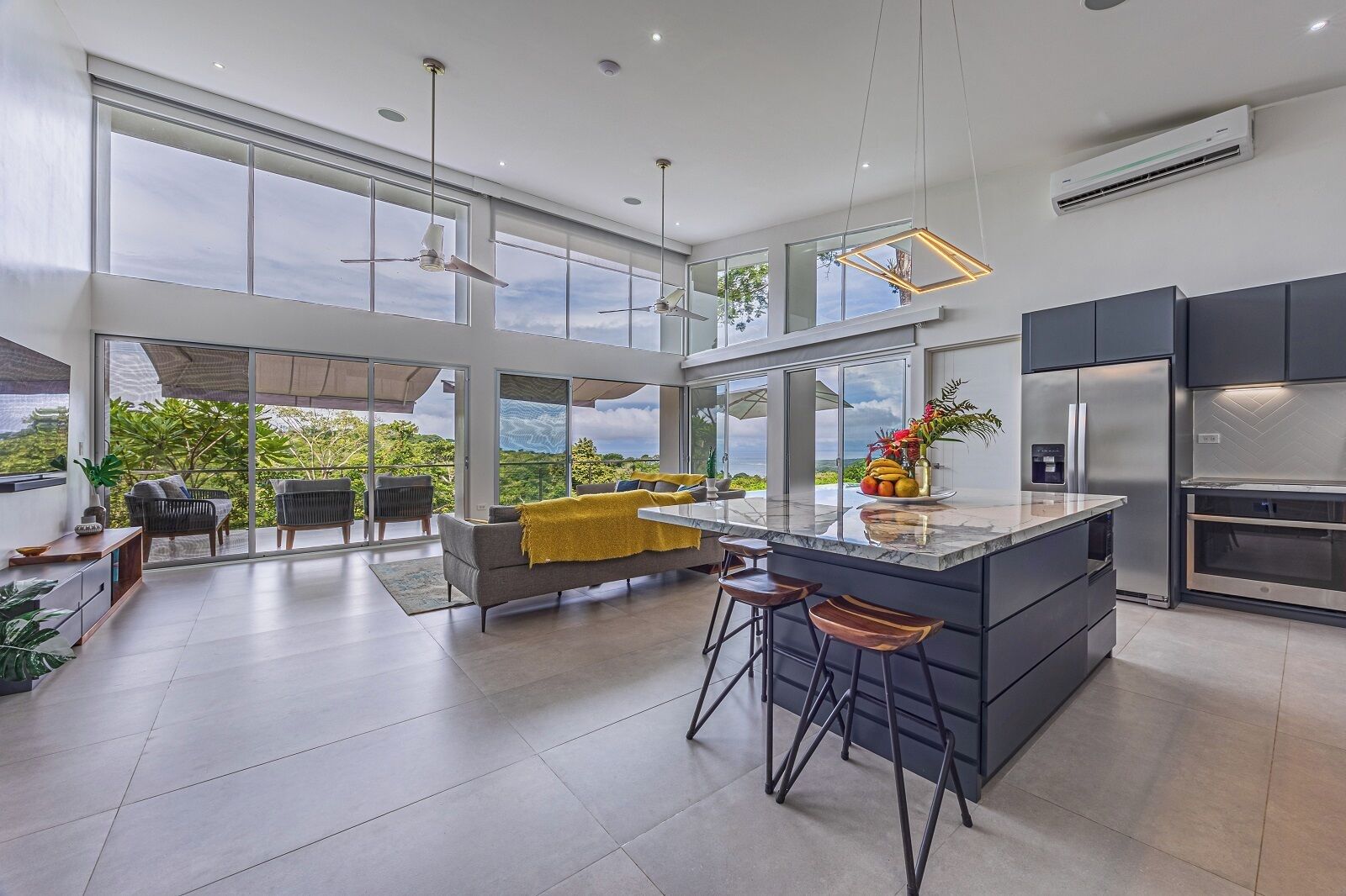 A modern kitchen with a large island, bar stools, and a view of greenery.