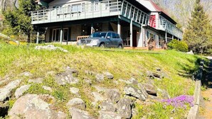 A two-story building with a balcony, a car parked in front, and a natural landscape with trees and rocks. - Catskill Cabin Apres Ski (Shandaken)