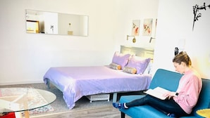 A room with a bed, a blue sofa, a round table, and a red chair. - Catskill Cabin Hummingbird Suite 2 (Shandaken)