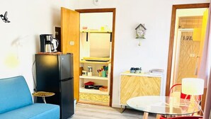 A compact living space with a blue sofa, a small round table, a red chair, a glass-top dining table, and a black refrigerator. - Catskill Cabin Hummingbird Suite 2 (Shandaken)