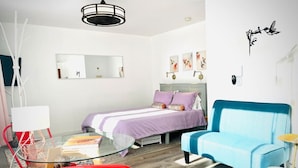A modern bedroom with a bed, a blue armchair, a glass table, and a red chair. - Catskill Cabin Hummingbird Suite 2 (Shandaken)