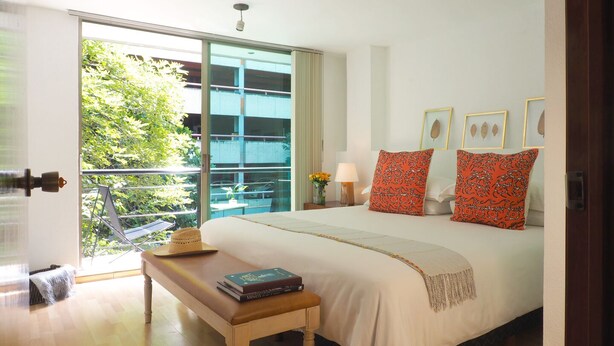 Un dormitorio con una cama grande, un banco, una mesita de noche con libros y vistas al exterior.