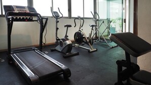 Un gimnasio con cintas de correr, bicicletas estáticas y un banco.