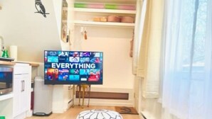Un salon avec un téléviseur affichant le mot « TOUT », une table basse en bois et une fenêtre avec des rideaux.