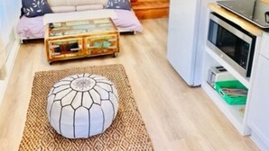 Un espace de vie compact comprenant un canapé, une table basse, un tapis, un coin cuisine avec un réfrigérateur et une table à manger avec des chaises.