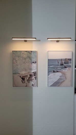 Two artworks adorn the wall, featuring dynamic beach scenes with waves and distinctive rock formations.