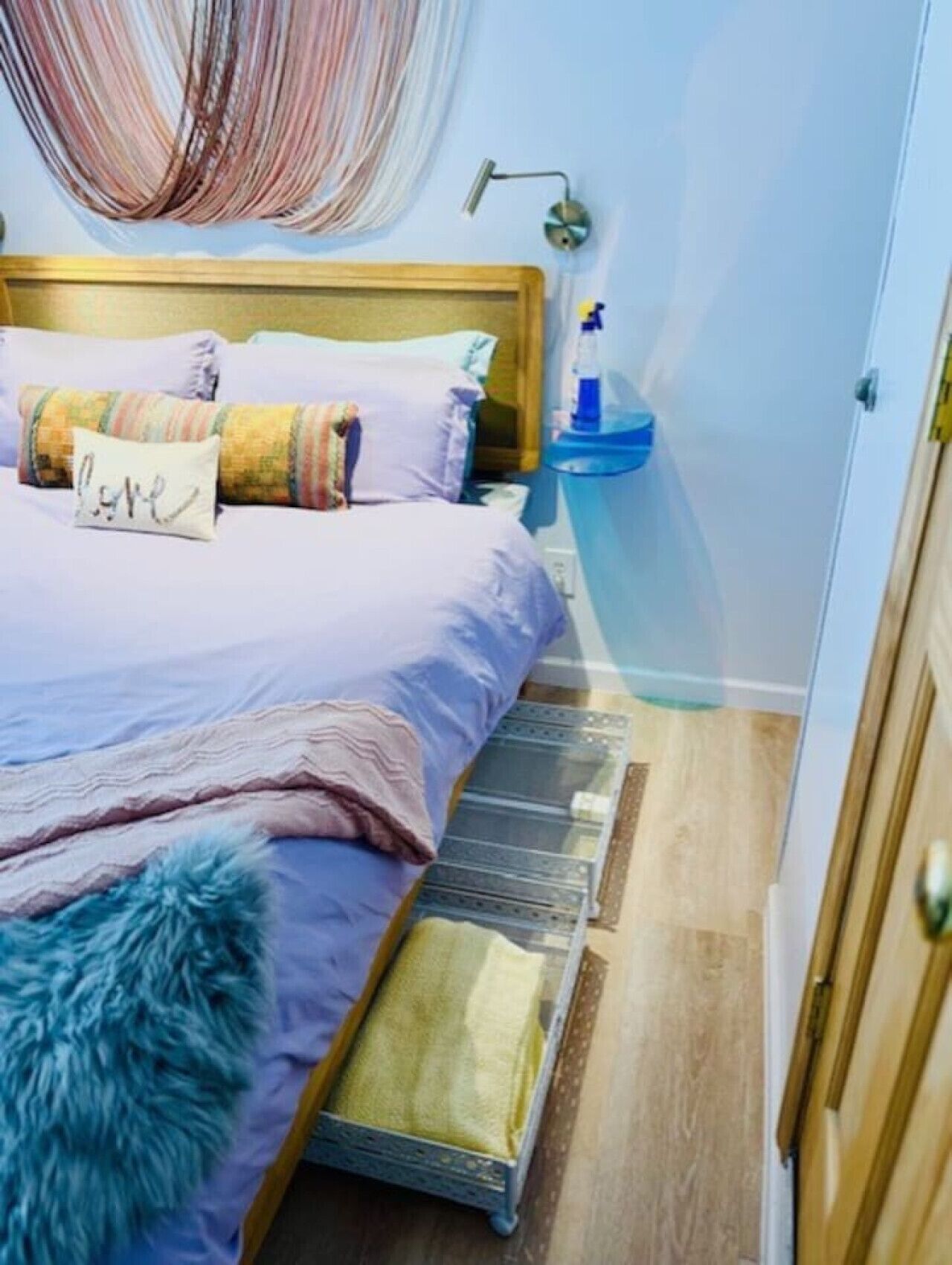 Een slaapkamer met een bed, kussens, een nachtkastje met een lamp en een klein vloerkleed.