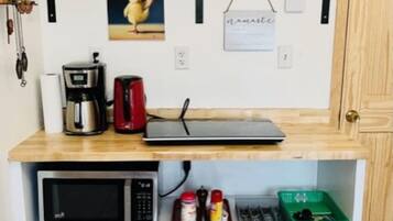 Eine kompakte Küche mit Mikrowelle, Kaffeemaschine und einer kleinen Arbeitsfläche.