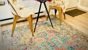 Une pièce avec un tapis à motifs floraux, une petite table ronde avec une lampe, deux chaises et un rideau rouge.