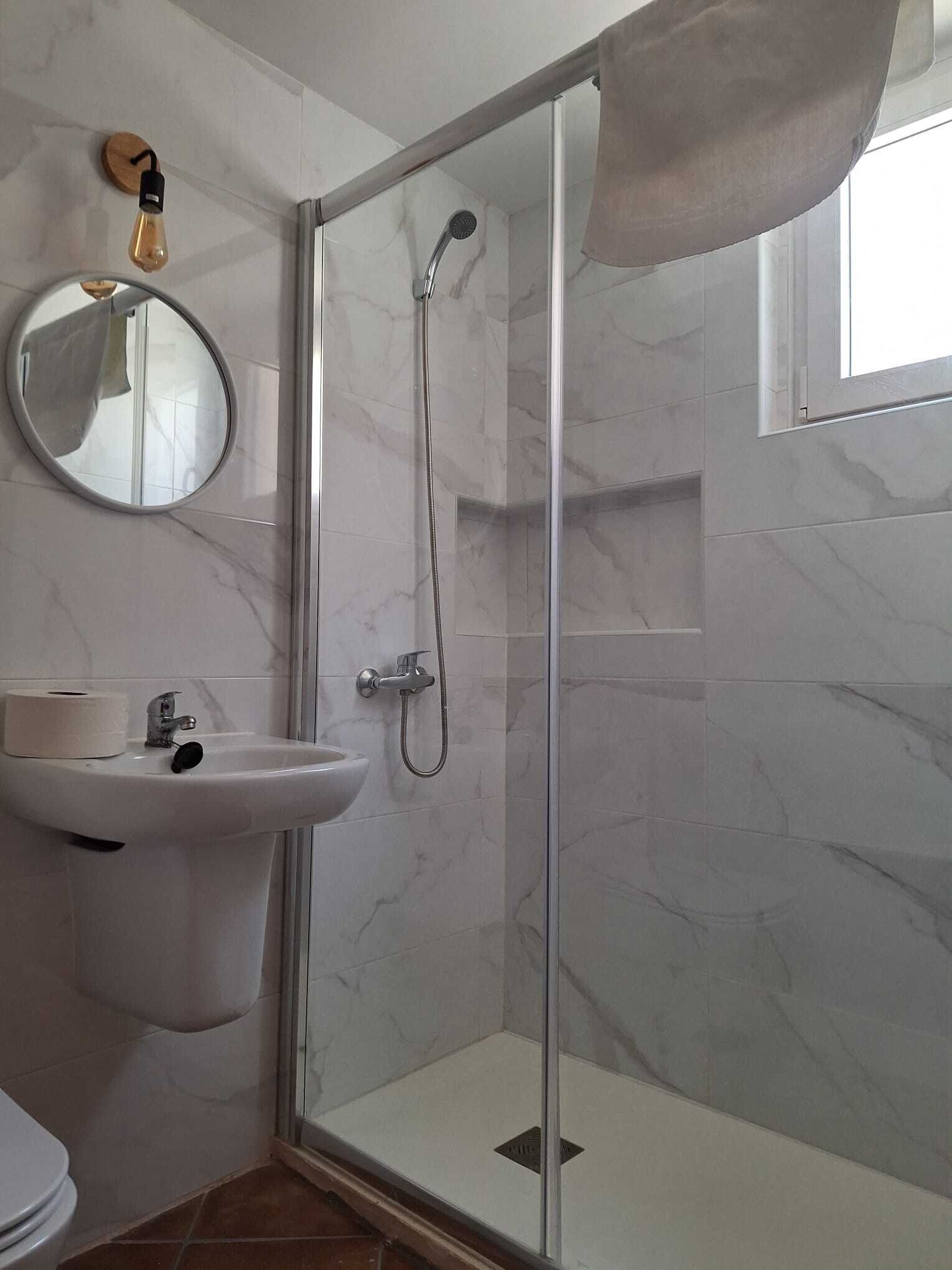 Een badkamer met een douchecabine van glas, een wastafel met spiegel en een toilet.
