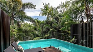 Un área junto a la piscina con maderas, sillones reclinables y barandilla de vidrio.