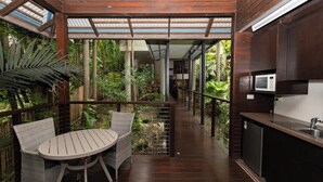 Un espacio al aire libre cubierto con una mesa y sillas, una zona de cocina con microondas, y una escalera que sube a un nivel superior.