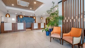 A hotel reception area with a wooden reception desk, two receptionists, and a large potted plant. - Flamingo Beach by Hilton: Oceanfront Resort, Pools & Spacious Studios To Relax! (Philipsburg)