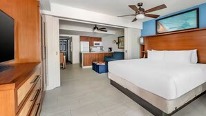 A hotel room with a large bed, a TV, a ceiling fan, and a view of the kitchen and living area. - Flamingo Beach by Hilton: Oceanfront Resort, Pools & Spacious Studios To Relax! (Philipsburg)