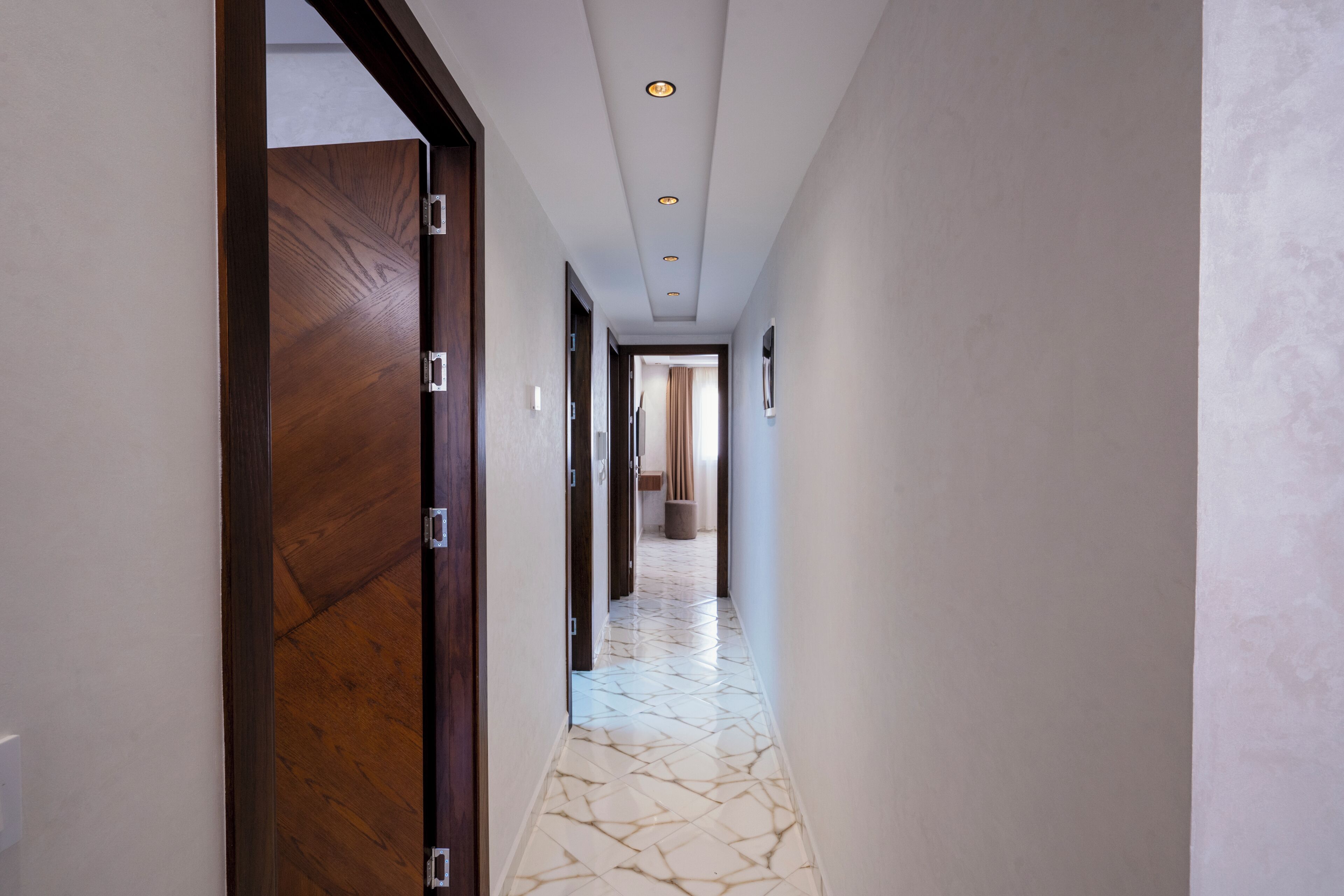 A hallway with a wooden door, recessed ceiling lights, and a patterned floor.