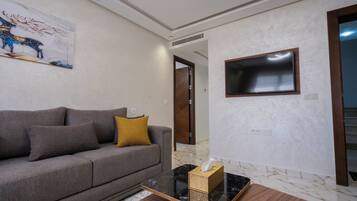 Una sala de estar con un sofá, una mesa de centro con una caja de pañuelos, un televisor montado en la pared y una puerta que da a otra habitación.
