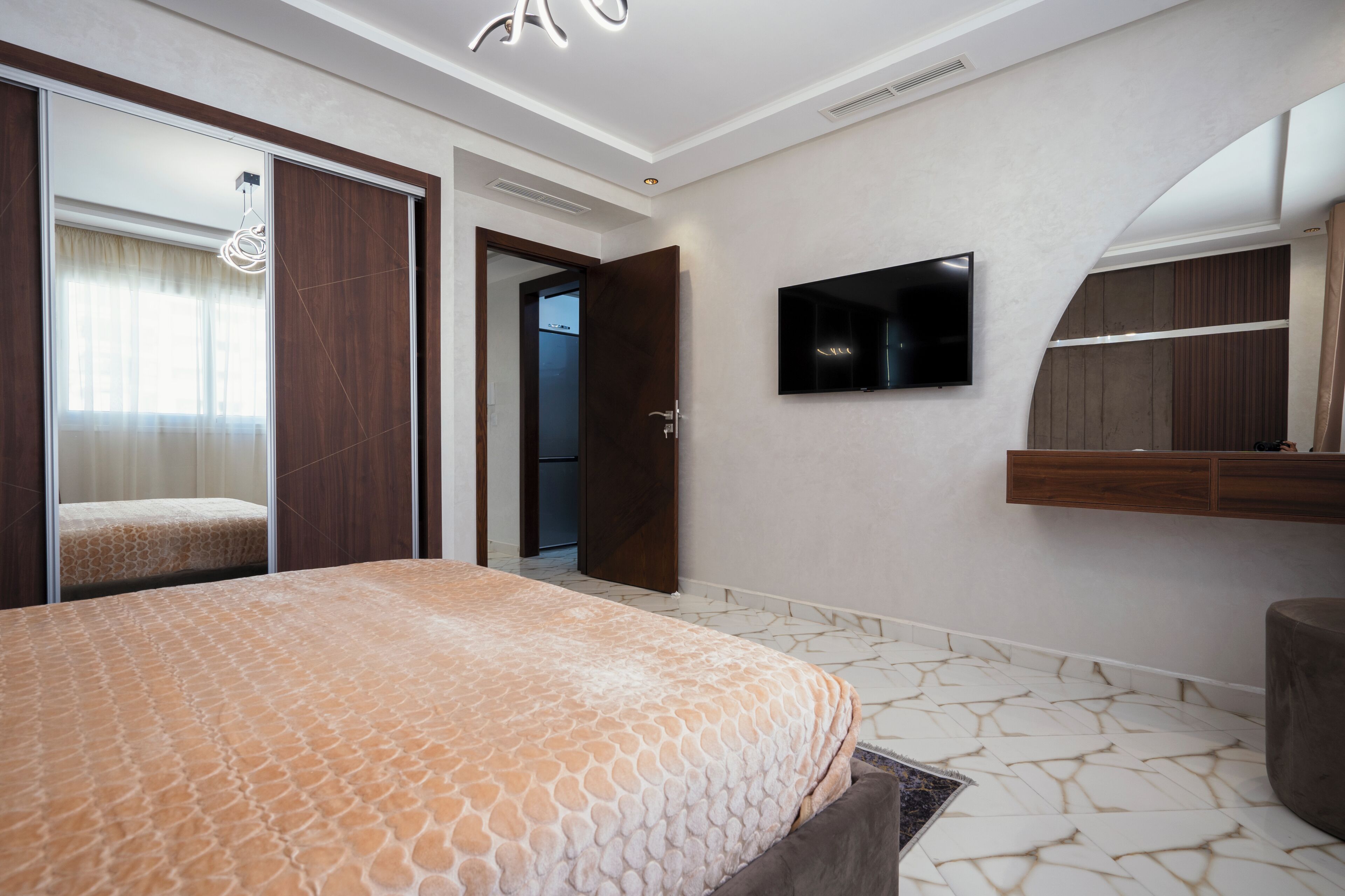A modern bedroom with a large bed, a TV mounted on the wall, and a wardrobe with a mirror.
