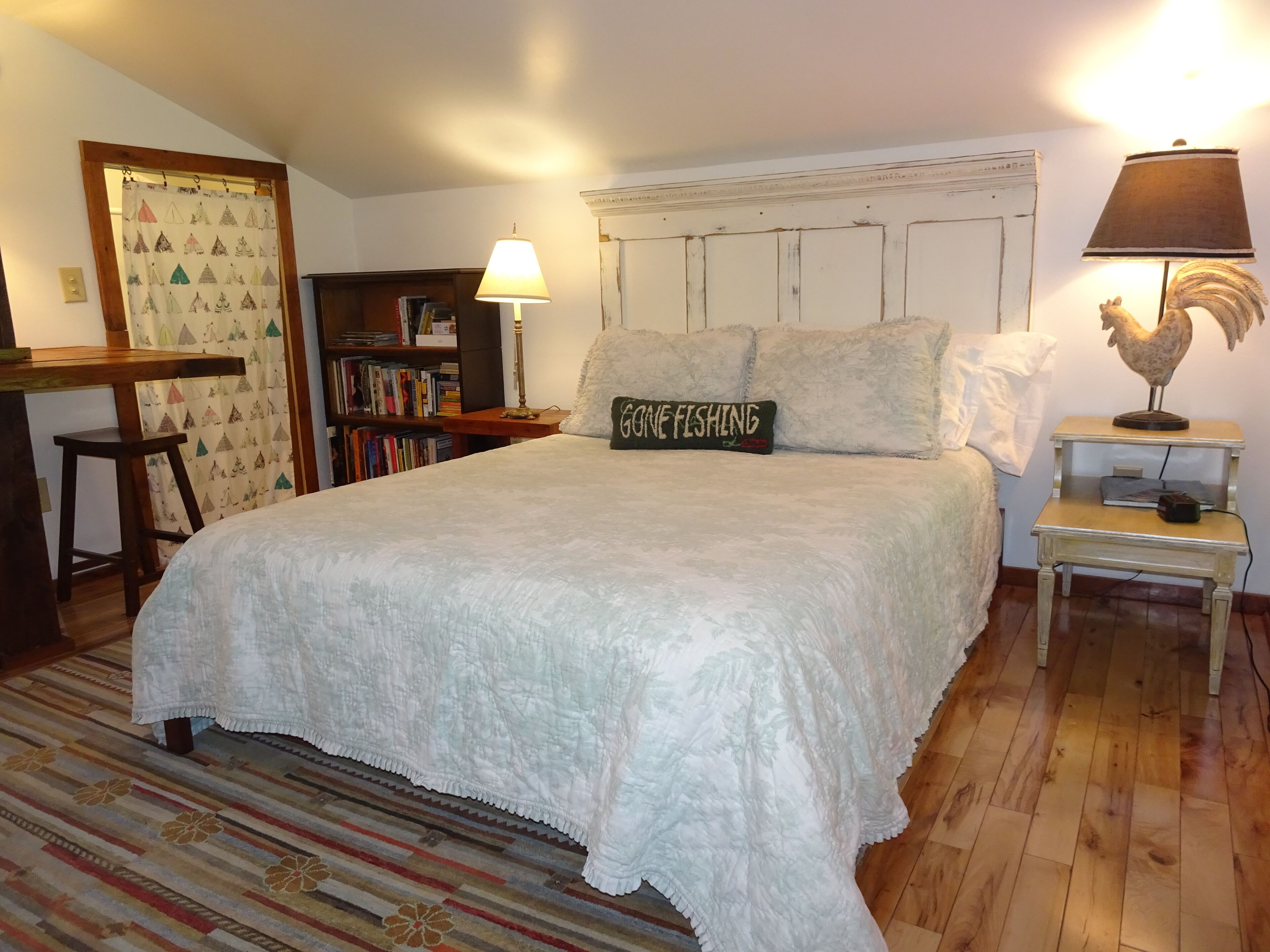 A bedroom with a large bed, a bookshelf, a lamp, and a decorative rooster.