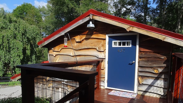 Eine Holzhütte mit blauer Tür, auf der die Nummer 437 steht, einem roten Dach und einer Holzterrasse.