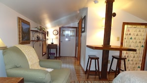 A cozy room with a green sofa, a wooden table, a bed with a white duvet, a patterned rug, and a door leading to another room. - Vogelsang guesthouse, 5 minute walk to downtown West Jefferson. (West Jefferson)