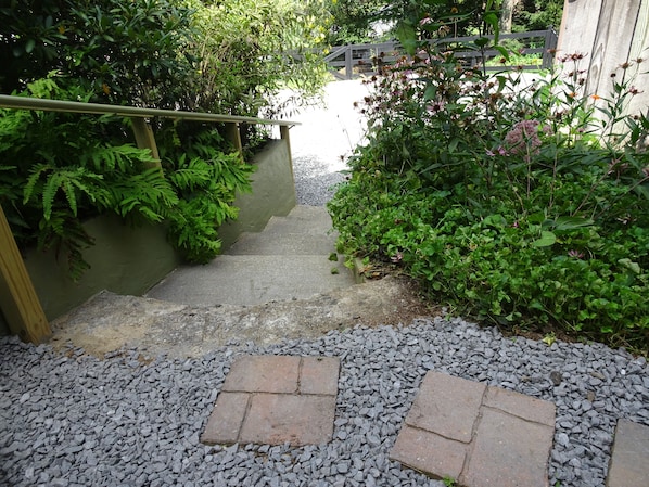A stone pathway leading up a set of stairs surrounded by lush greenery and a wooden fence.